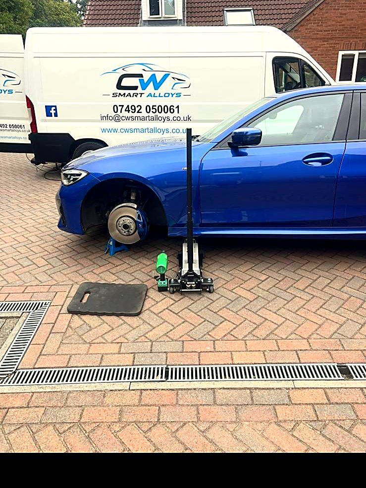 Blue BMW 3 Series jacked up with wheels off beside the CW Smart Alloys vans